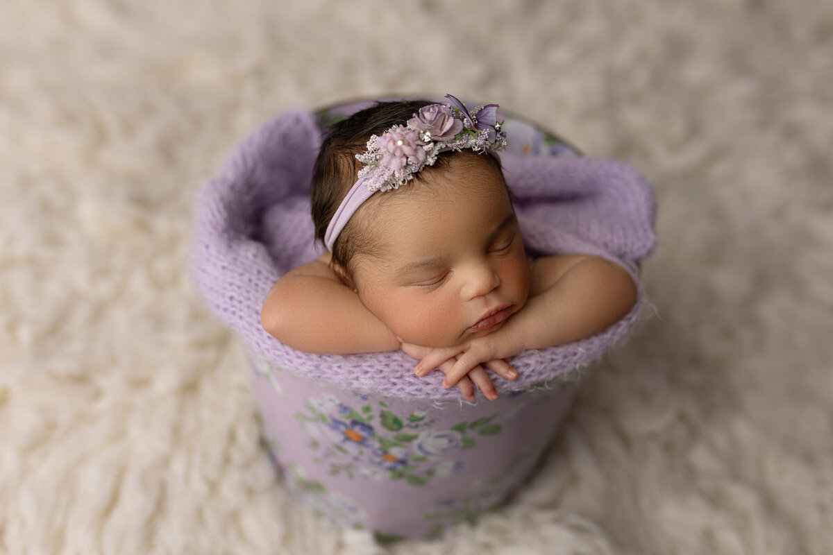 Newborn baby girl in a light purple bucket 
