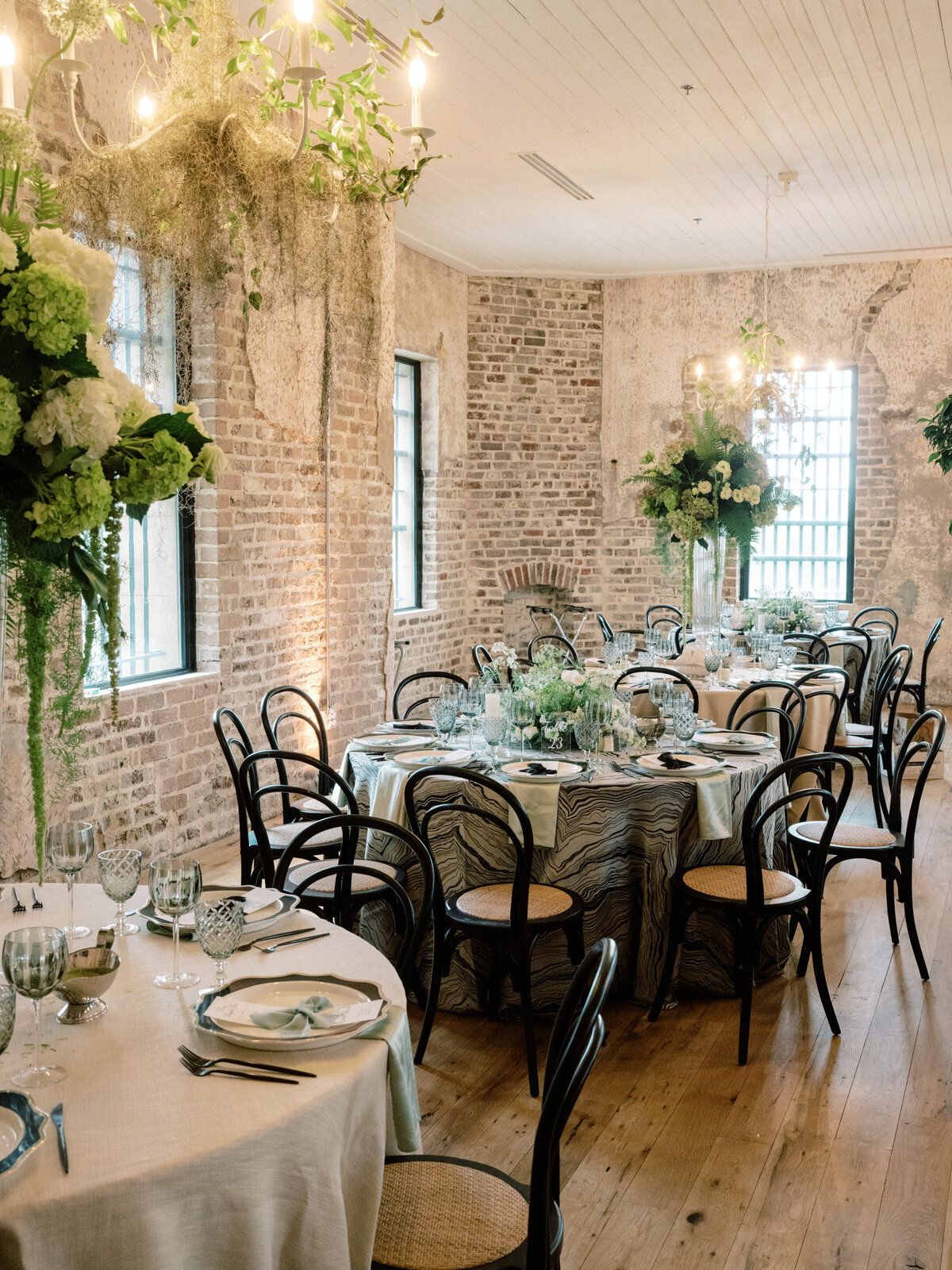 This image showcases a beautifully decorated indoor wedding space featuring elegant tables, lush greenery, and soft lighting that creates an ambient atmosphere.