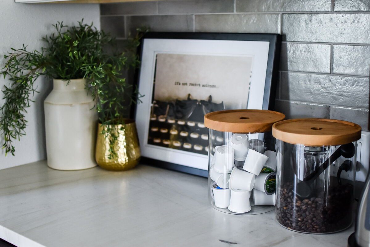 Two glass storage canisters hold coffee and k cups on a kitchen counter