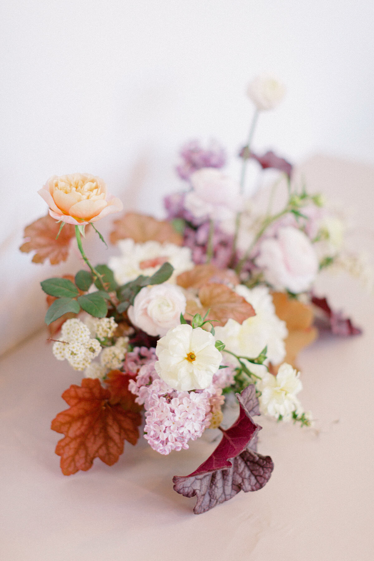 An arrangement of spring flowers featuring lilacs and colourful greenery sits on a table.