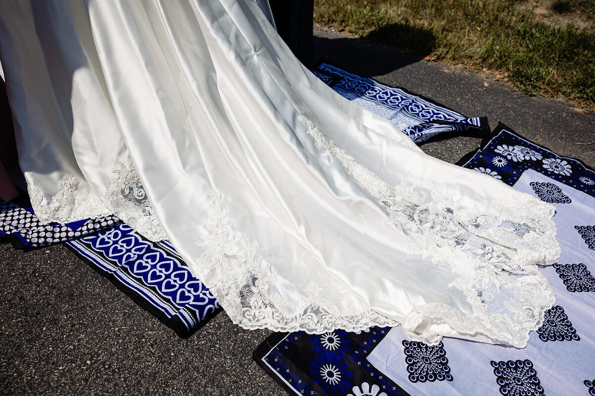 Close-up of a bride's elegant white wedding gown with detailed lace hemline displayed on a traditional blue and white patterned fabric