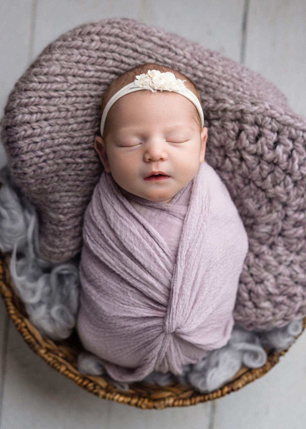 newborn baby wrapped in a purple fabric asleep in a brown bowl