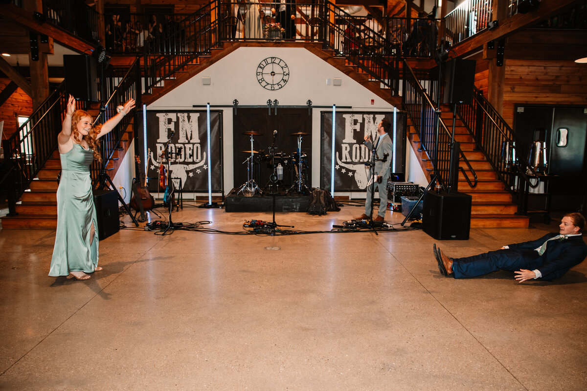 A groomsman lays on the ground while dancing with a bridesmaid during their reception entrance