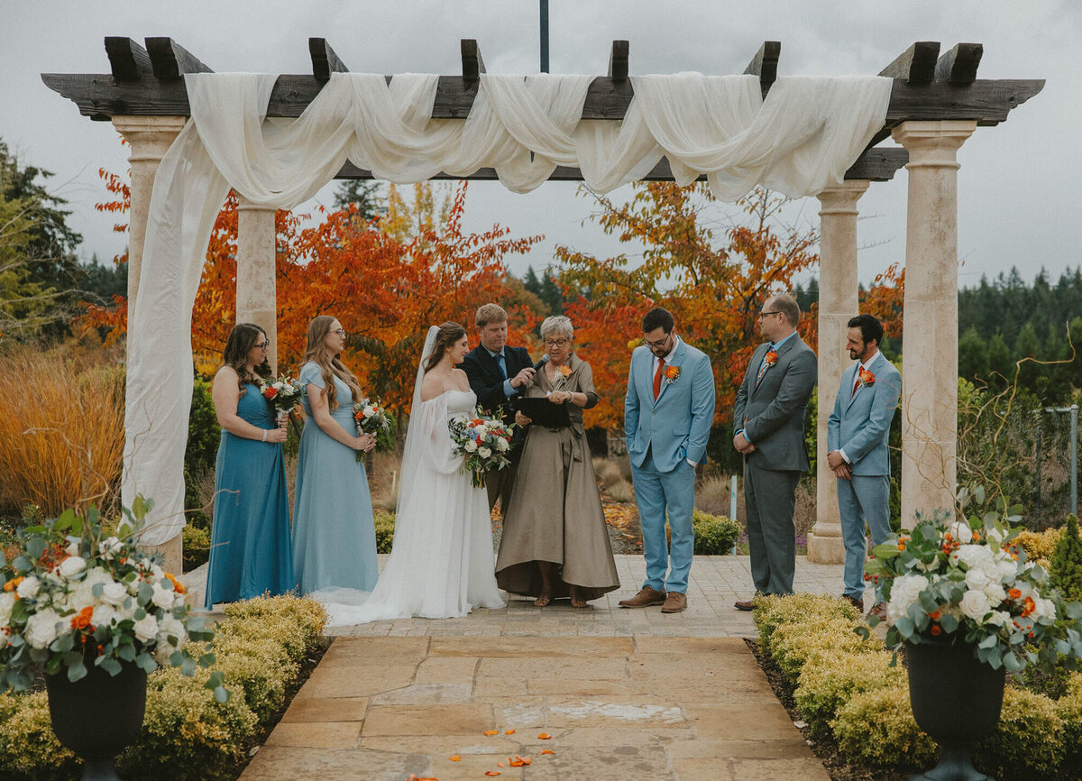 The wedding party standing under a arbor drapes with white fabric at a wedding planned by Birdie June Events.