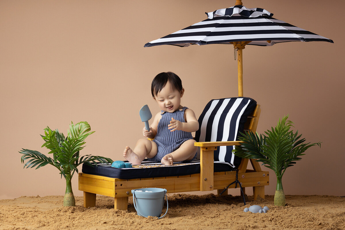 Dallas baby milestone photographer capturing a baby playing with a shovel and bucket on the beach.