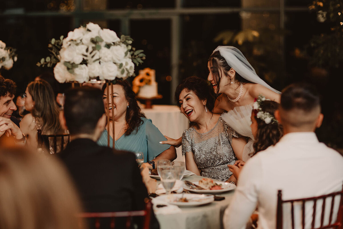 A newlywed laughing with a table of wedding guests 