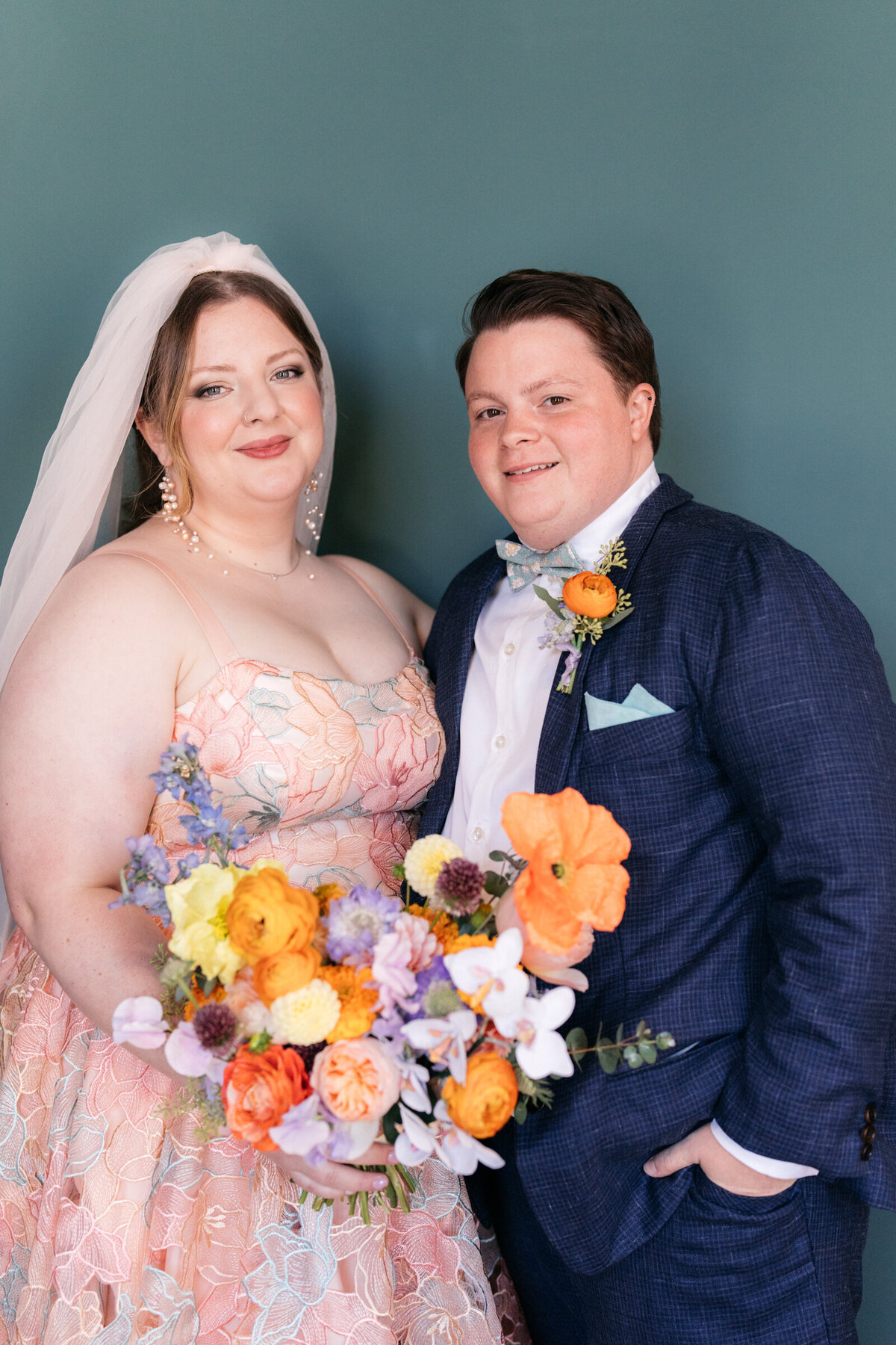 bride wearing colorful wedding dress standing with groom in front of teal backdrop
