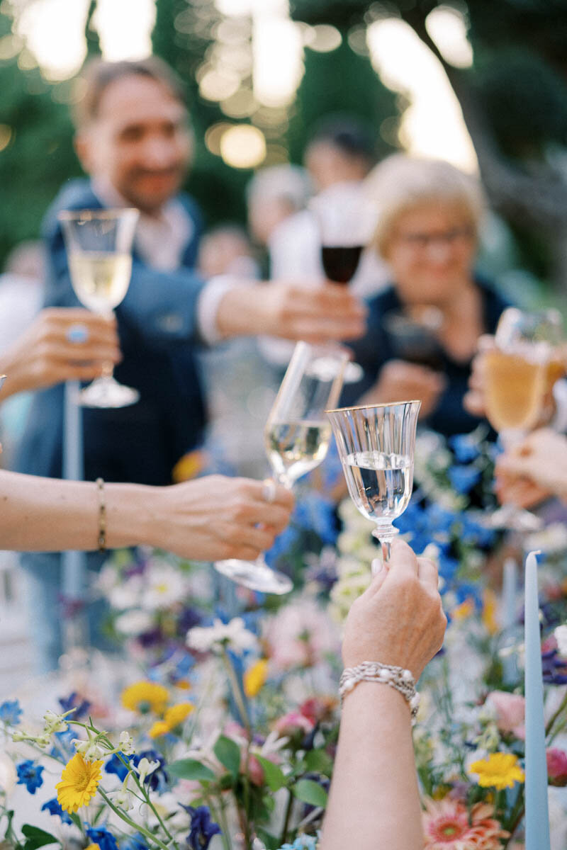 Close-up of guests raising glasses during a joyful wedding reception toast, surrounded by colorful floral arrangements