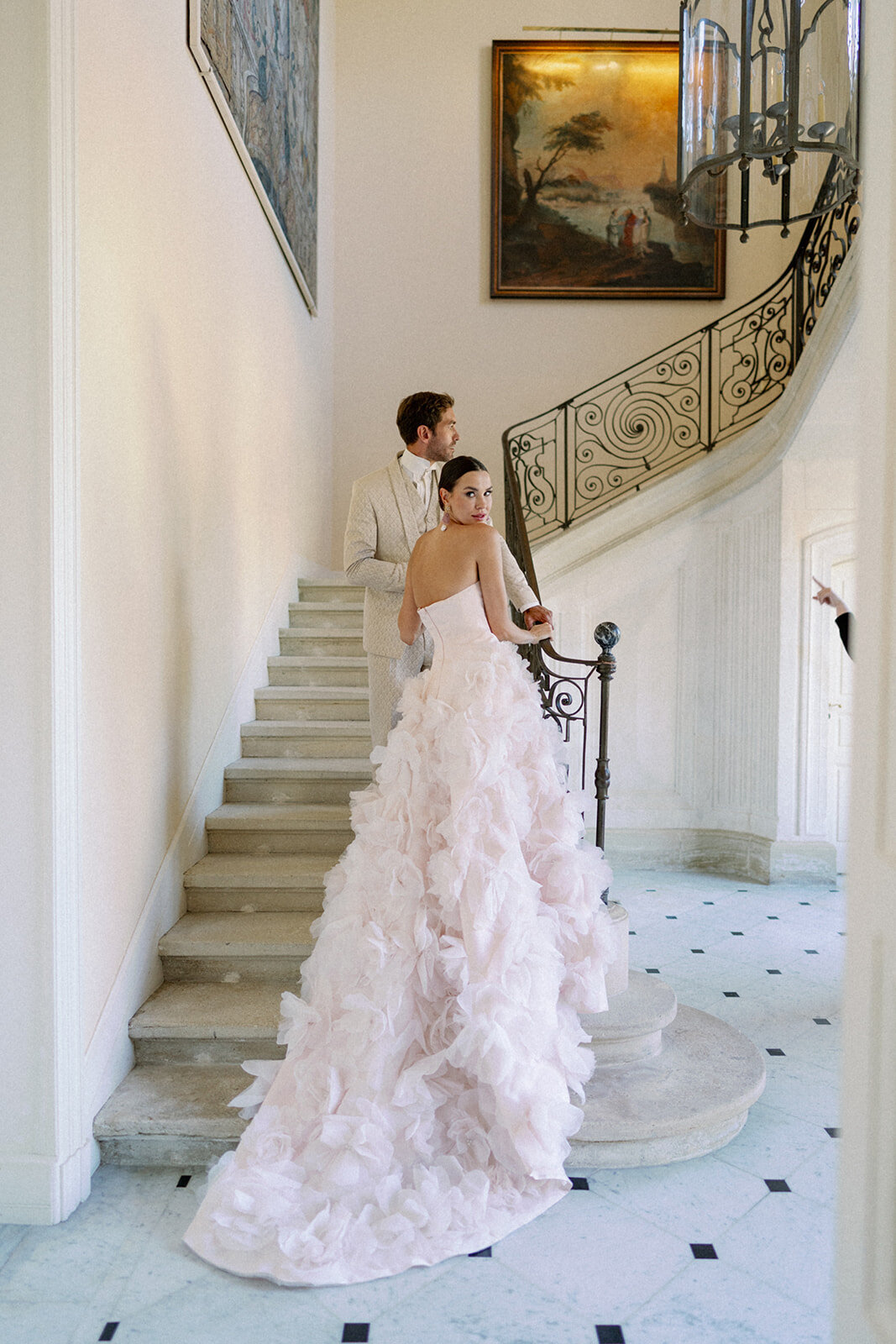 Bride posing on grand stone staircase in a blush textured gown inside Château de Tourreau in Provence France.