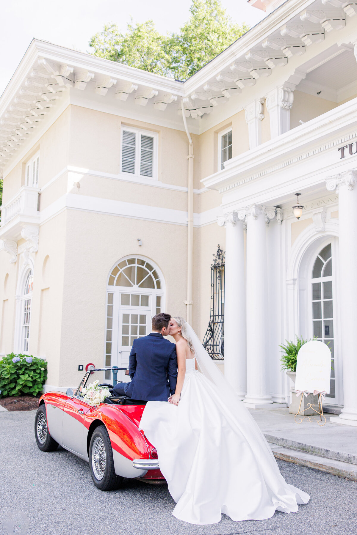 Bride and groom kissing while sitting on a vintage car during their Tupper Manor wedding pictures