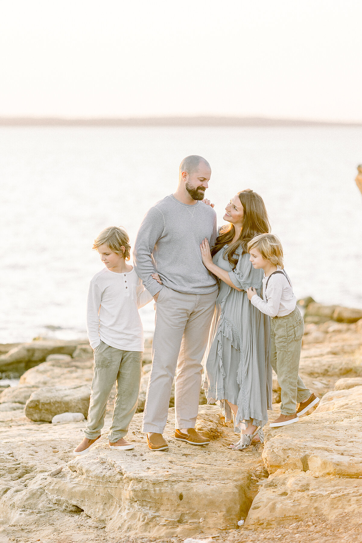 A Frisco Tx Family posing by a lake on the rocks for family photos.