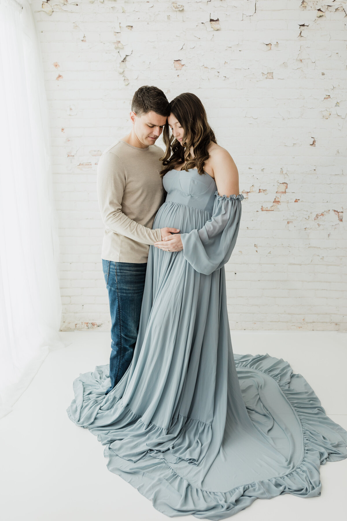 husband and pregnant wife in blue maternity gown holding baby bump for maternity photoshoot
