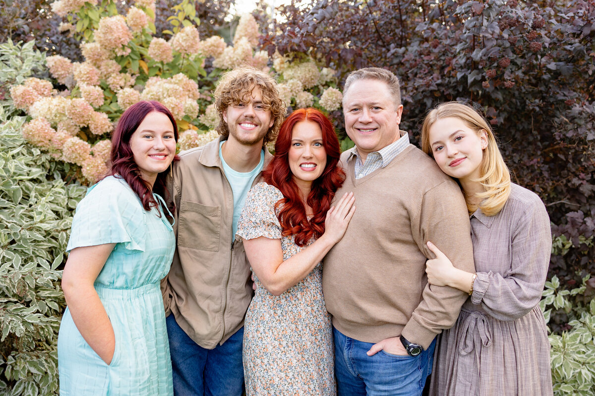 A family of five standing in front of vibrant blooming flowers, dressed in coordinated outfits for a timeless family portrait.