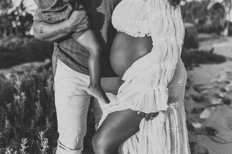 Close-up black-and-white maternity photo of parents holding their child while highlighting the mother’s baby bump — emotional Oahu maternity photography by Leslie Carbajal Photography