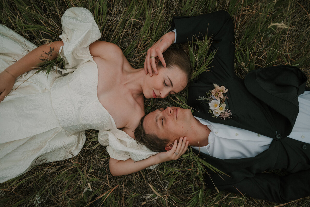 bride and groom laying in grass and holding each others faces