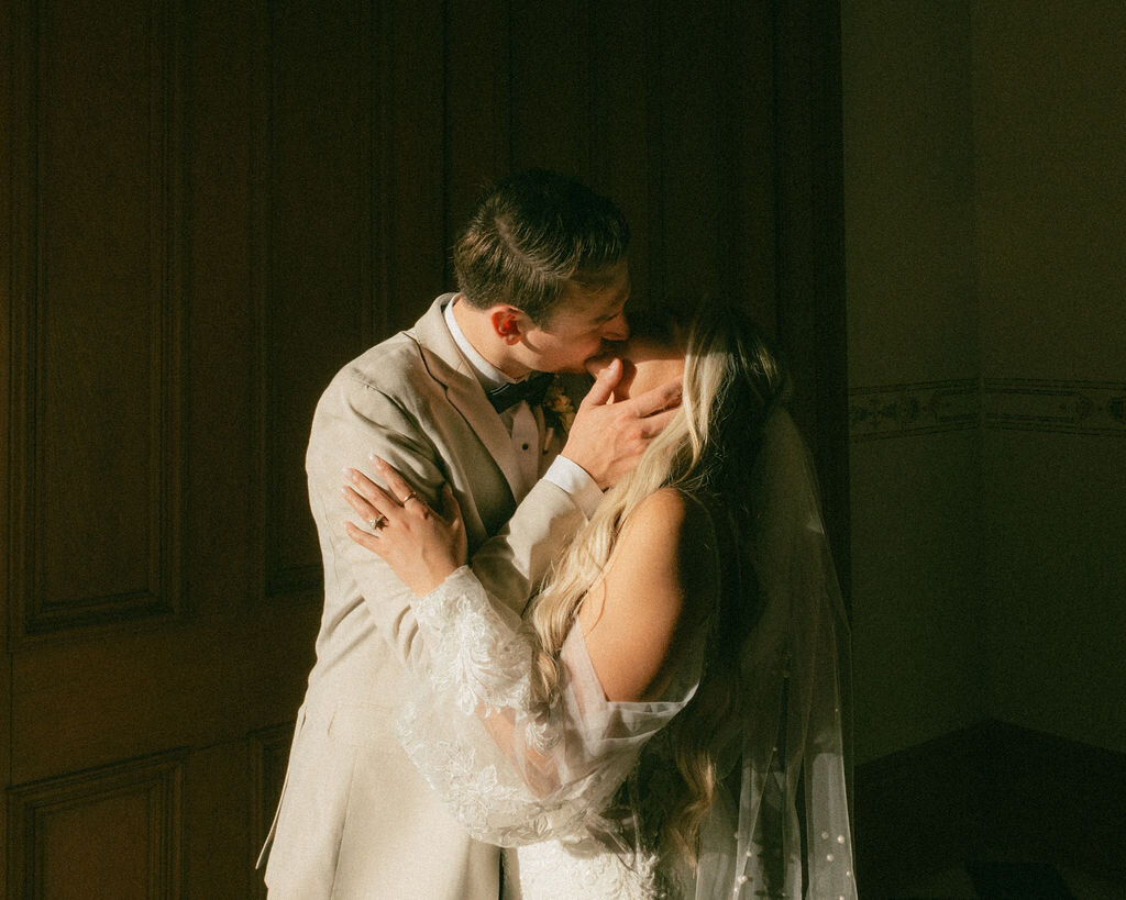 Groom hugs bride from behind and kisses her cheek