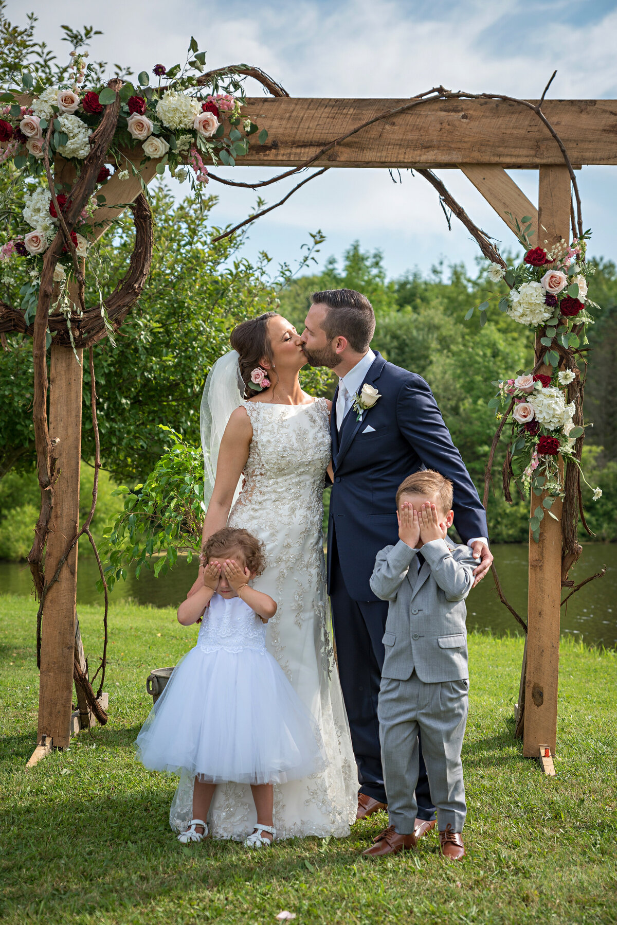 Bride and groom kiss while ring bearer and flower girl cover eyes.