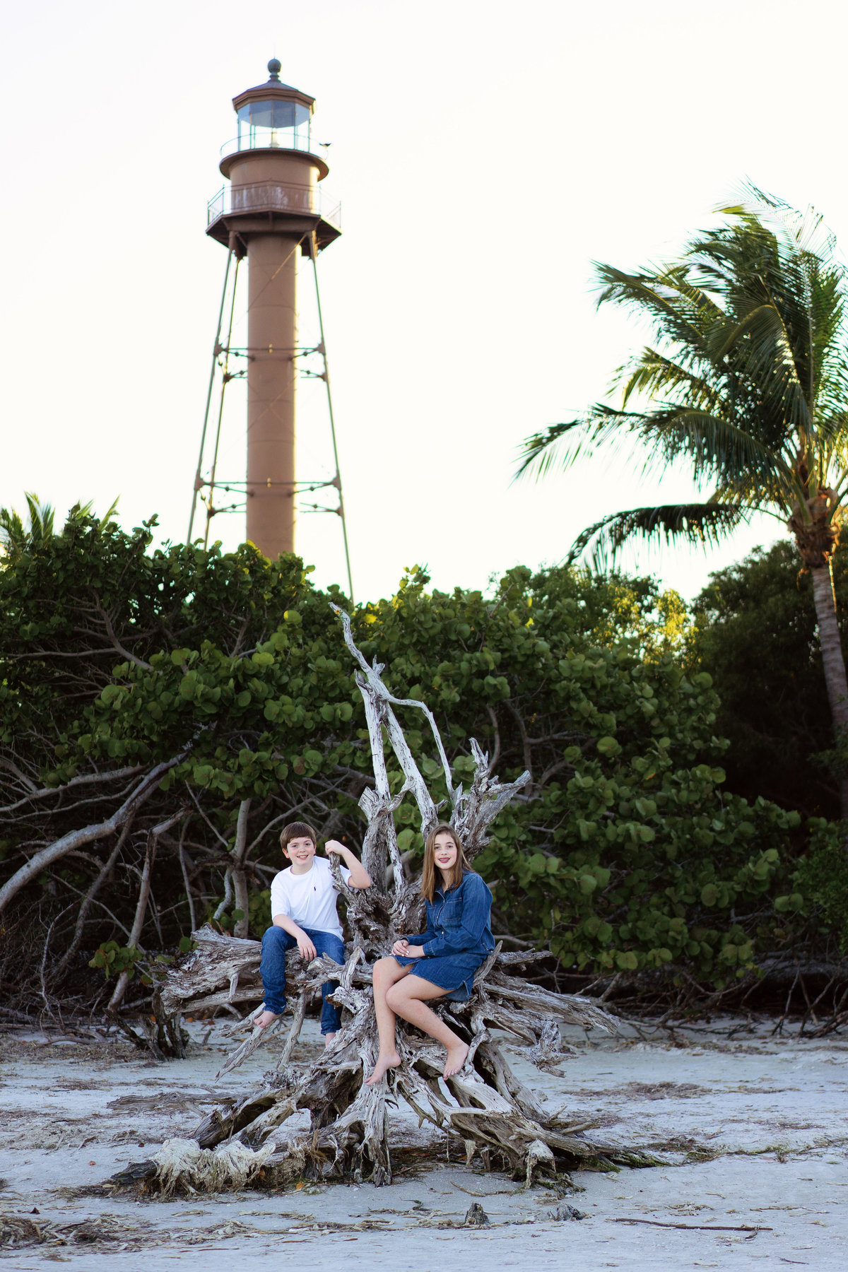 Brother and sister at Lighthouse Beach on Sanibel sitting on driftwood in front of the lighthouse