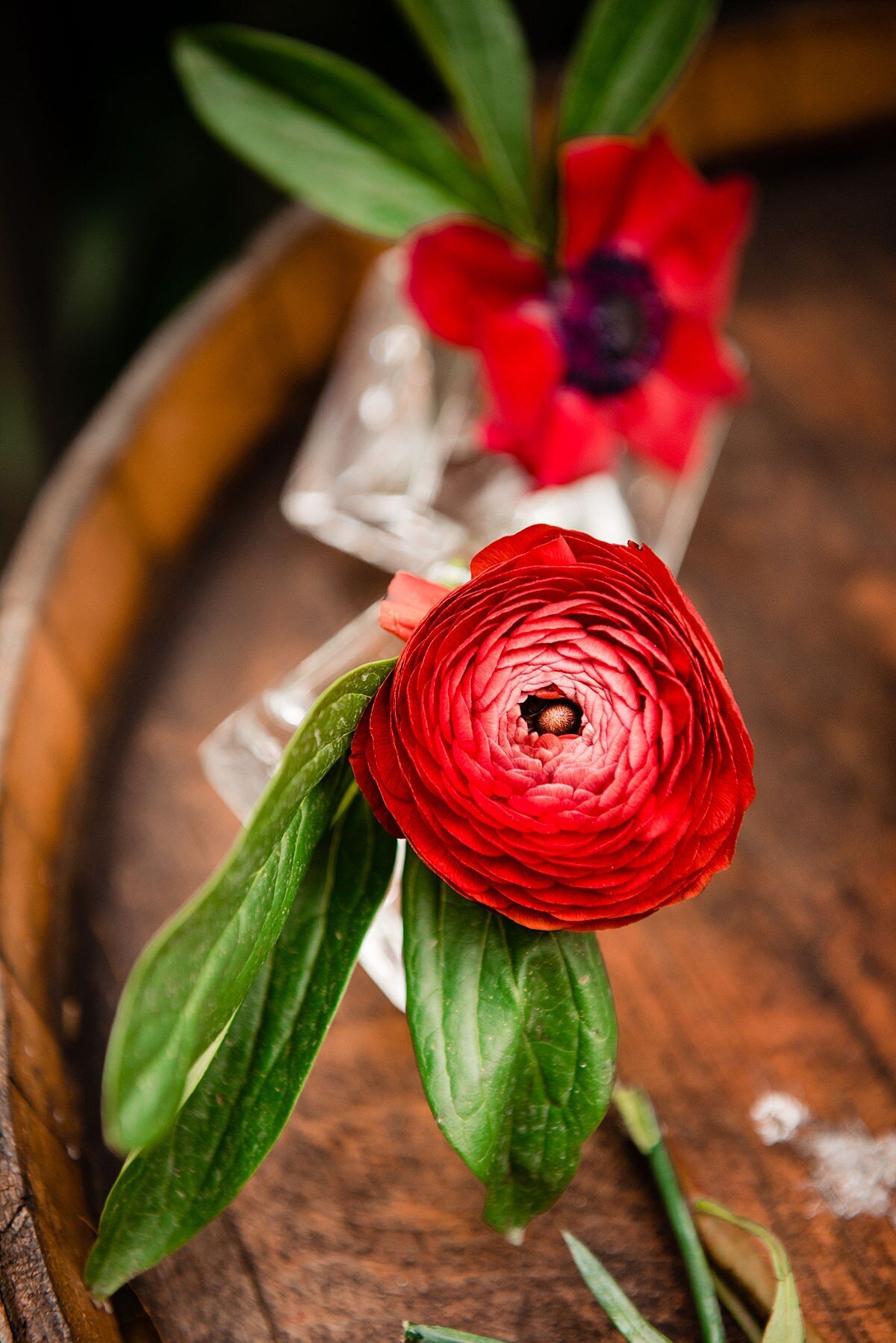 Red ranunculus and red anemones in square glass bud vases sitting on top of a wine barrel at a summer wedding at Arrington Vineyards.