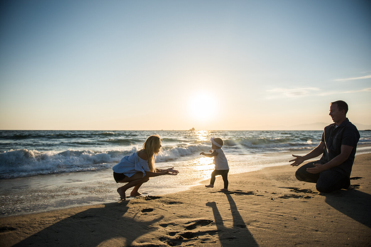 A parent stands with arms wide as a child runs up to them on the beach.