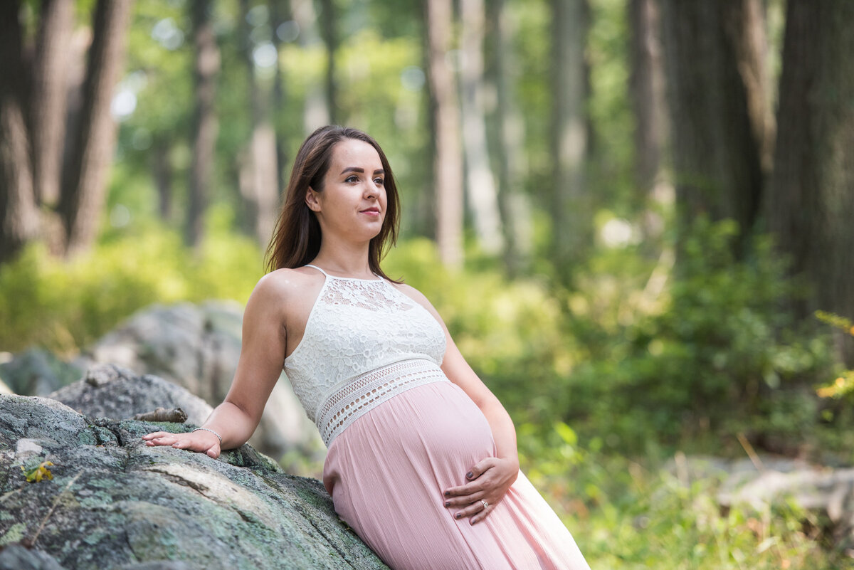 A person leaning against a rock holding their pregnant stomach