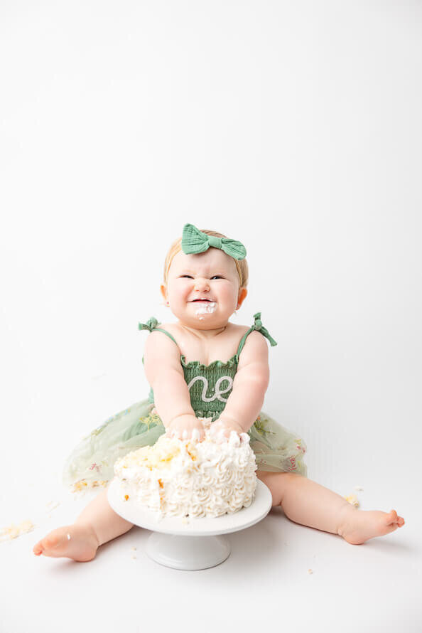 One year old girl smiles at camera and smashes her cake.