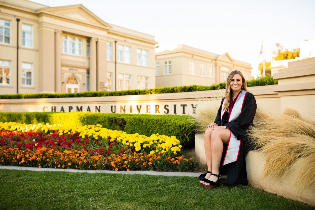 Chapman University graduate sits in front of her school while wearing her graduation gown