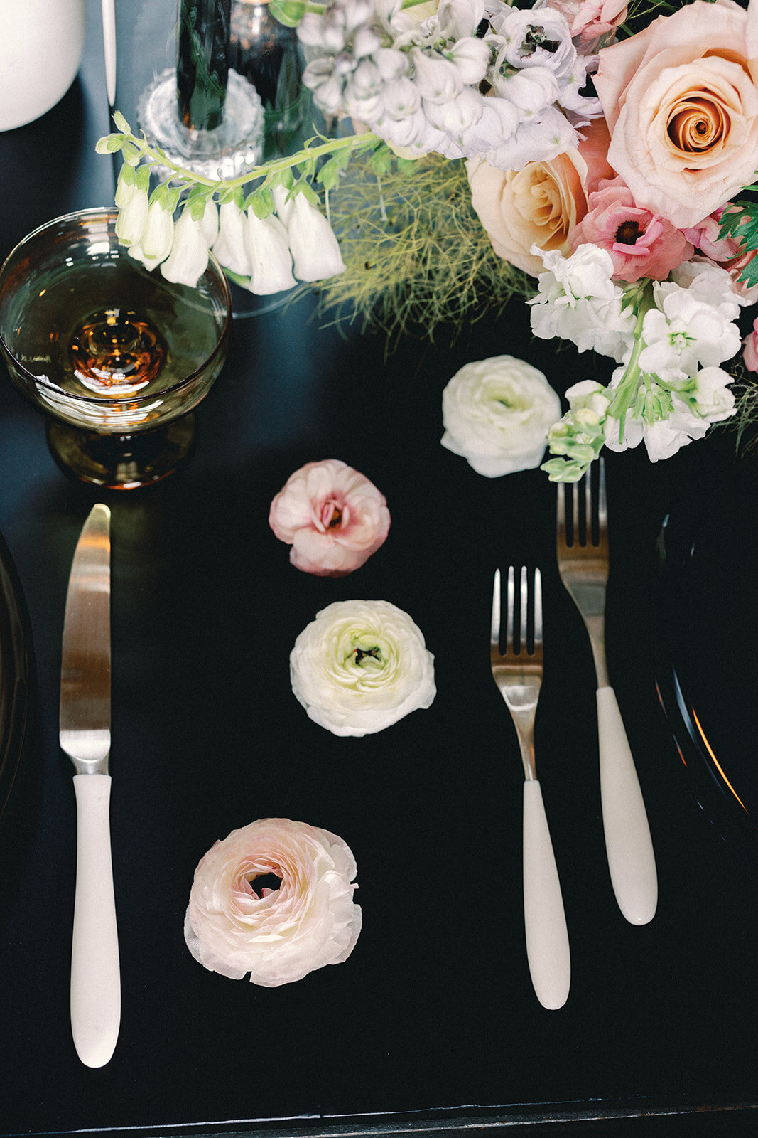 Silverware and pink and white flowers on a black table