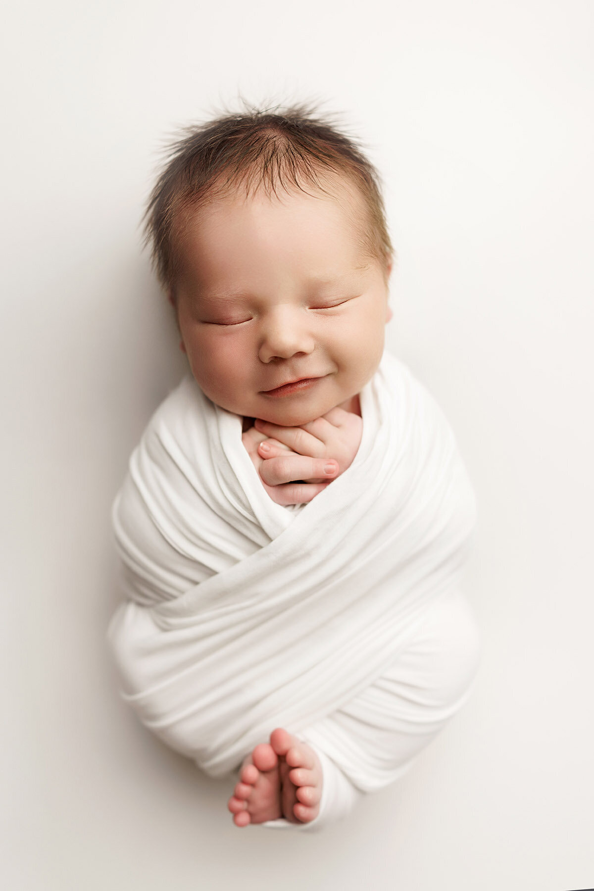 Wrapped up baby boy in all white smiling