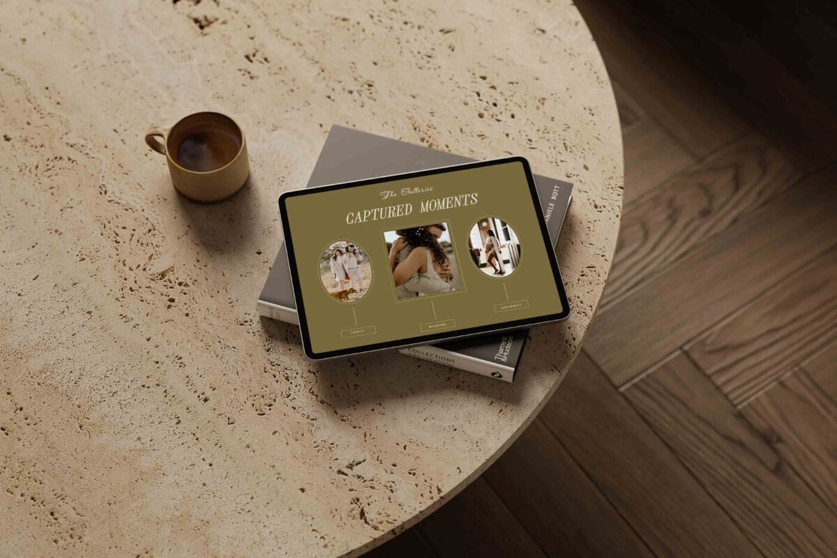 Tablet resting on stacked books and a round stone coffee table beside a beige coffee cup, displaying a photography website page titled “Captured Moments” with three circular image categories: family, wedding, and maternity