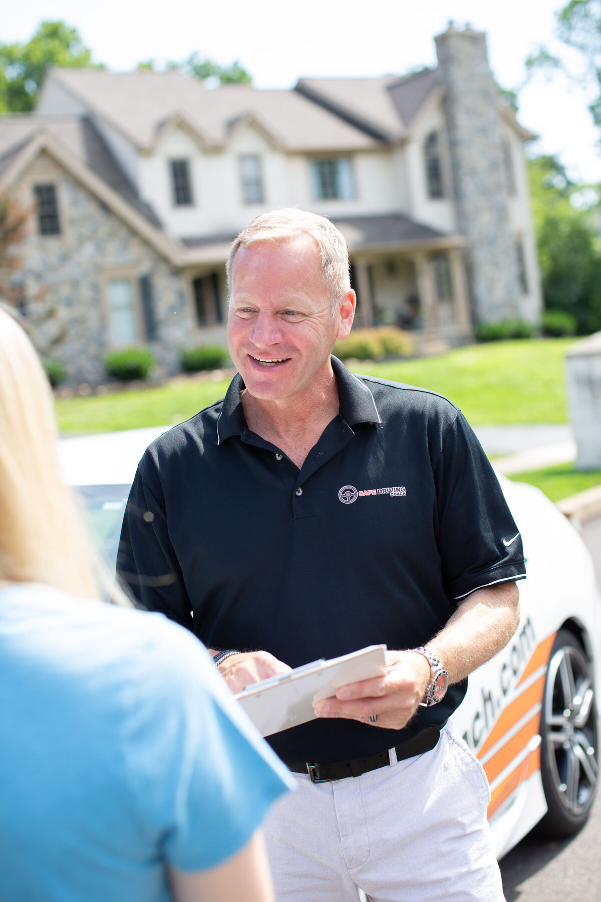 Driving coach smiling at student, car in background