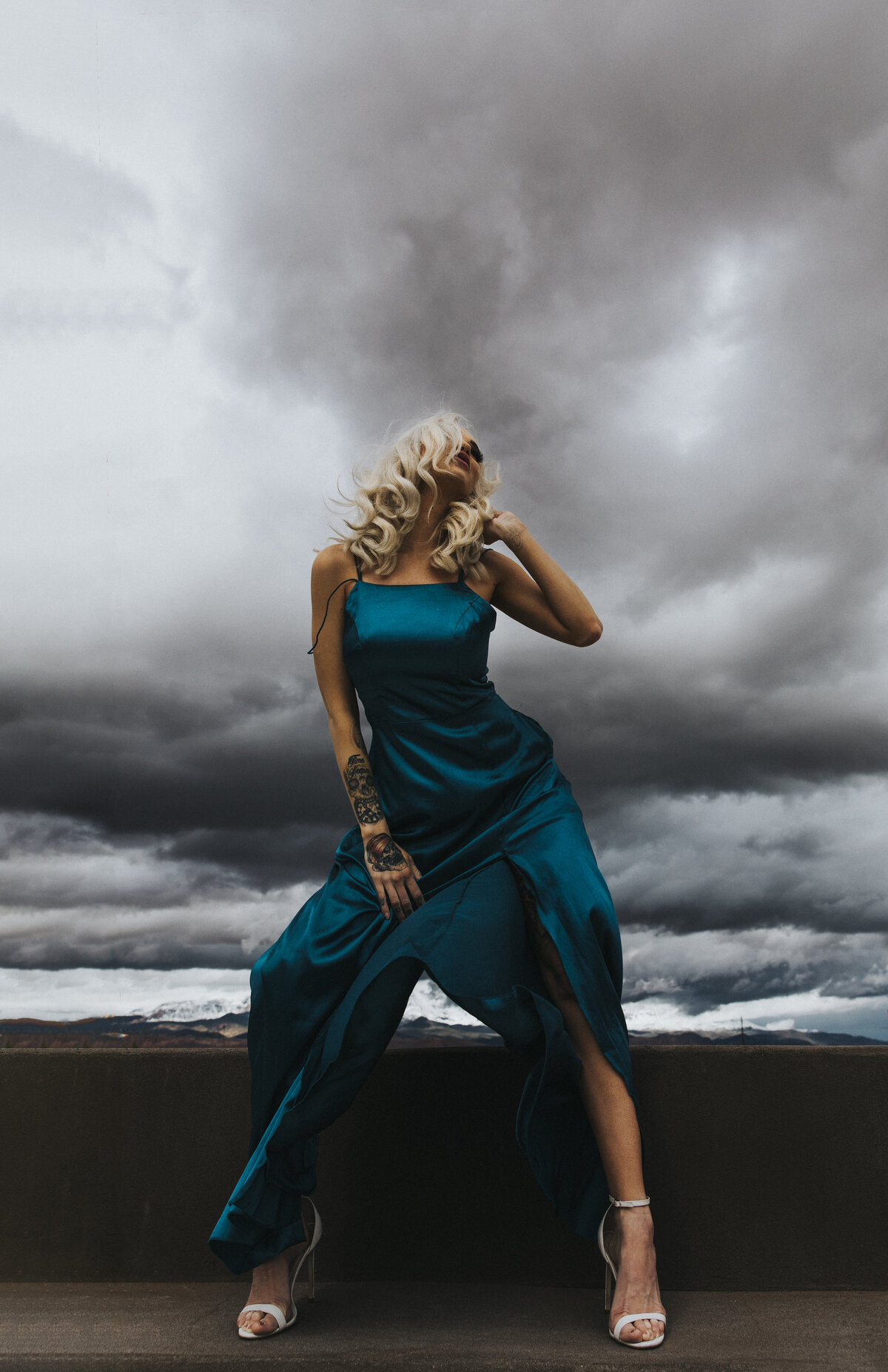A woman in a blue dress is  standing in the wind of a strom