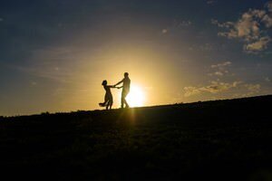 Romantic couple silhouette at sunset captured by St Augustine wedding photographers, showing two people holding hands on a hill against golden sky