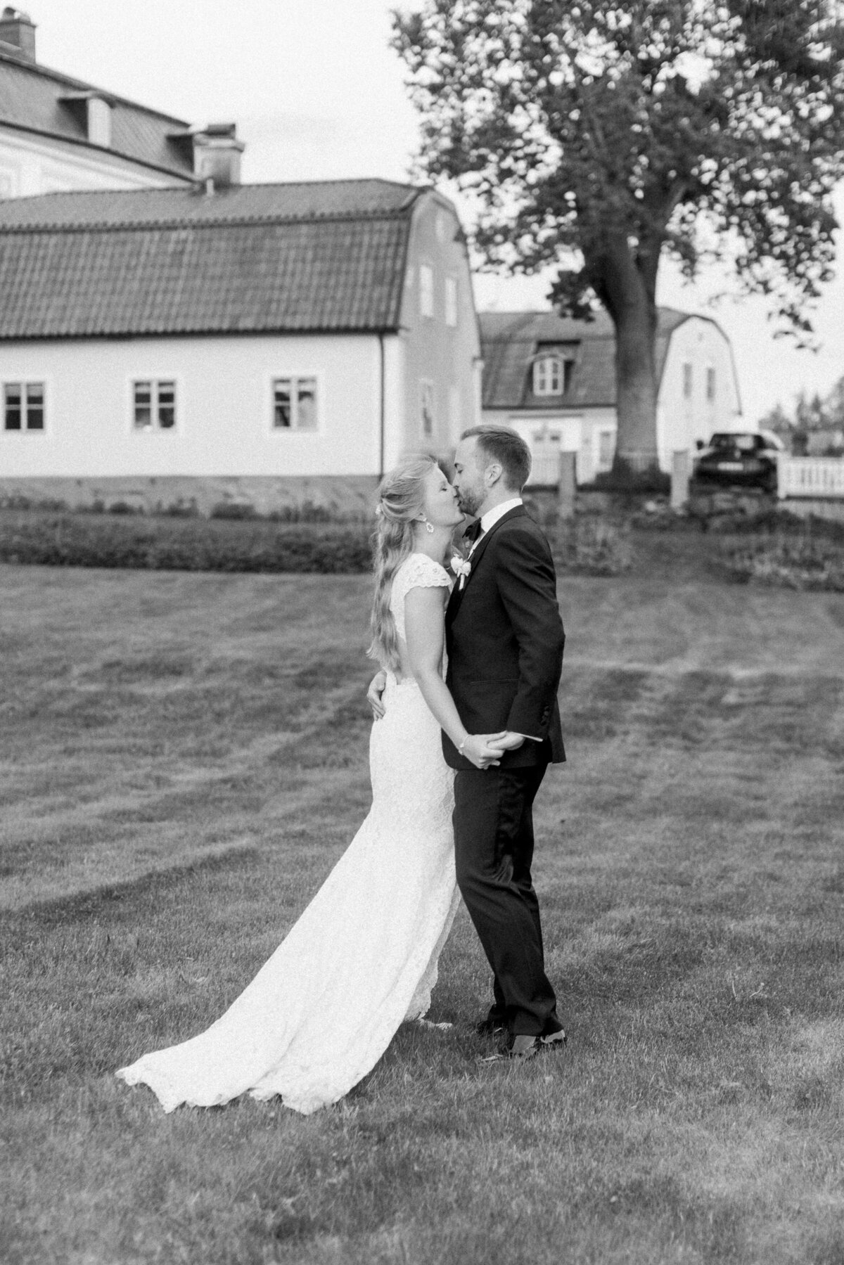 Bröllopspar kysser varandra på gräsmattan utanför Schenströmska