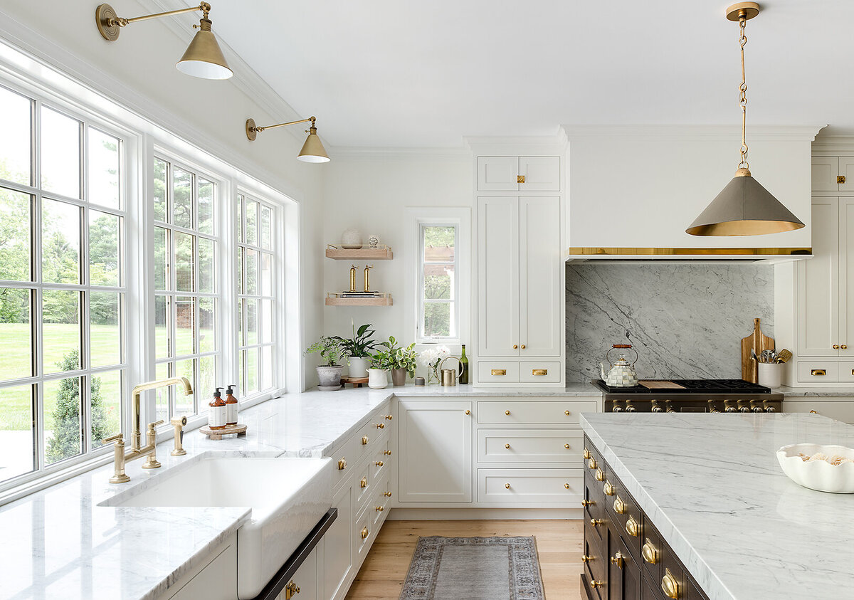 bright white kitchen with gold and dark wood accents, marble countertop and large windows