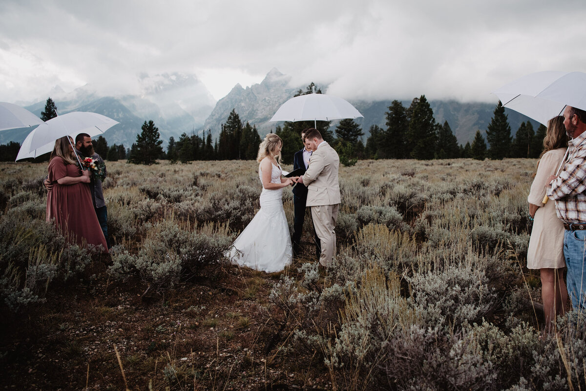 wyoming elopement in the grand tetons with bride adn groom exchanging rings under a white umbrella for rainy day wedding captured by jackson hole wedding  photographers