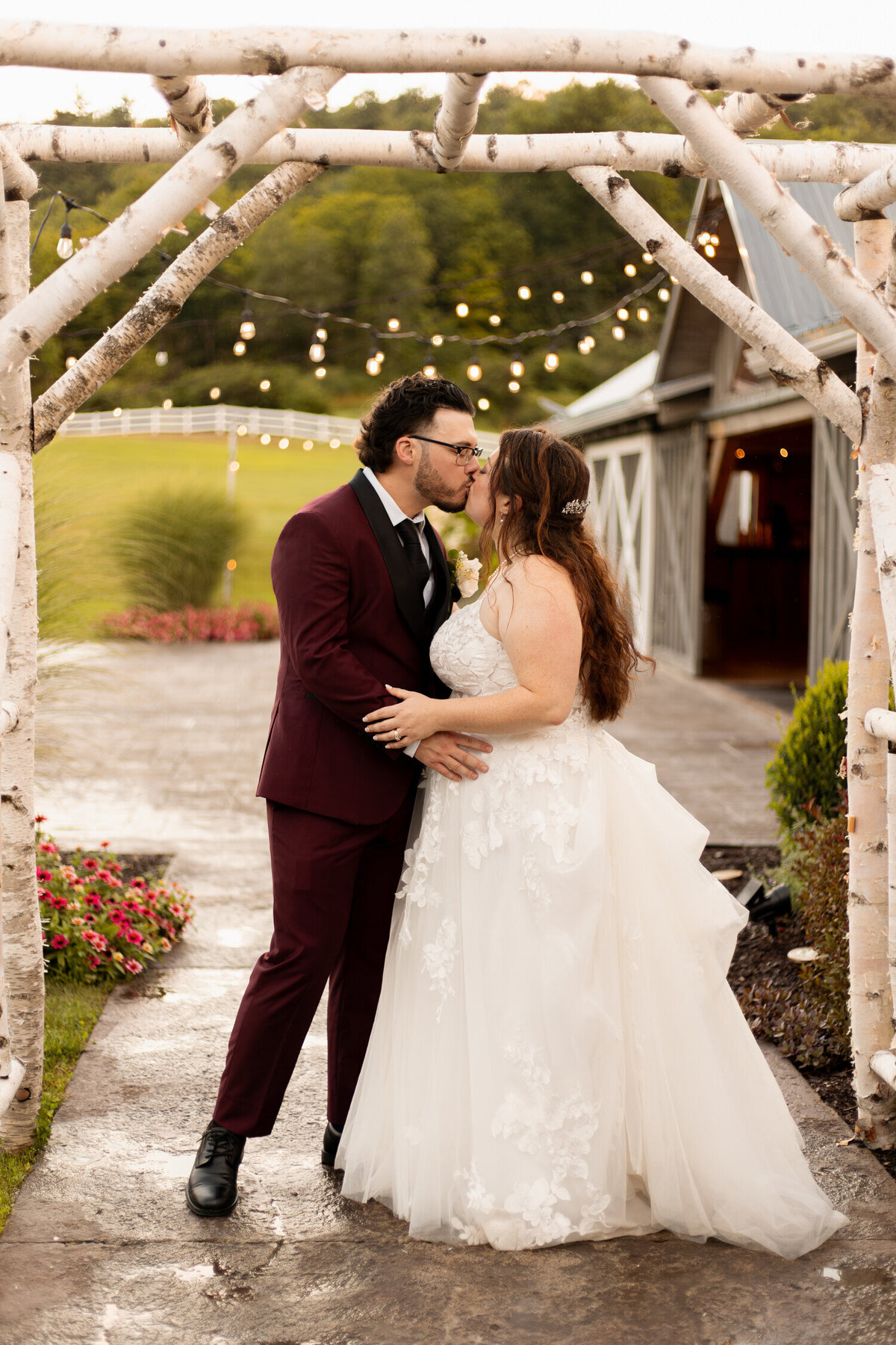 A bride and groom share a kiss underneath an arch during their wedding at the The Barn at Lord Howe in Ticonderoga, NY.