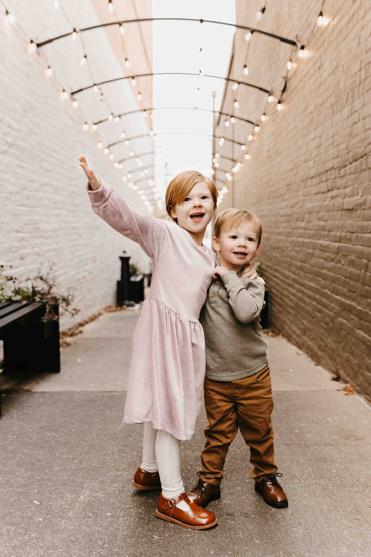 Big sister and little brother with arms around each other laughing