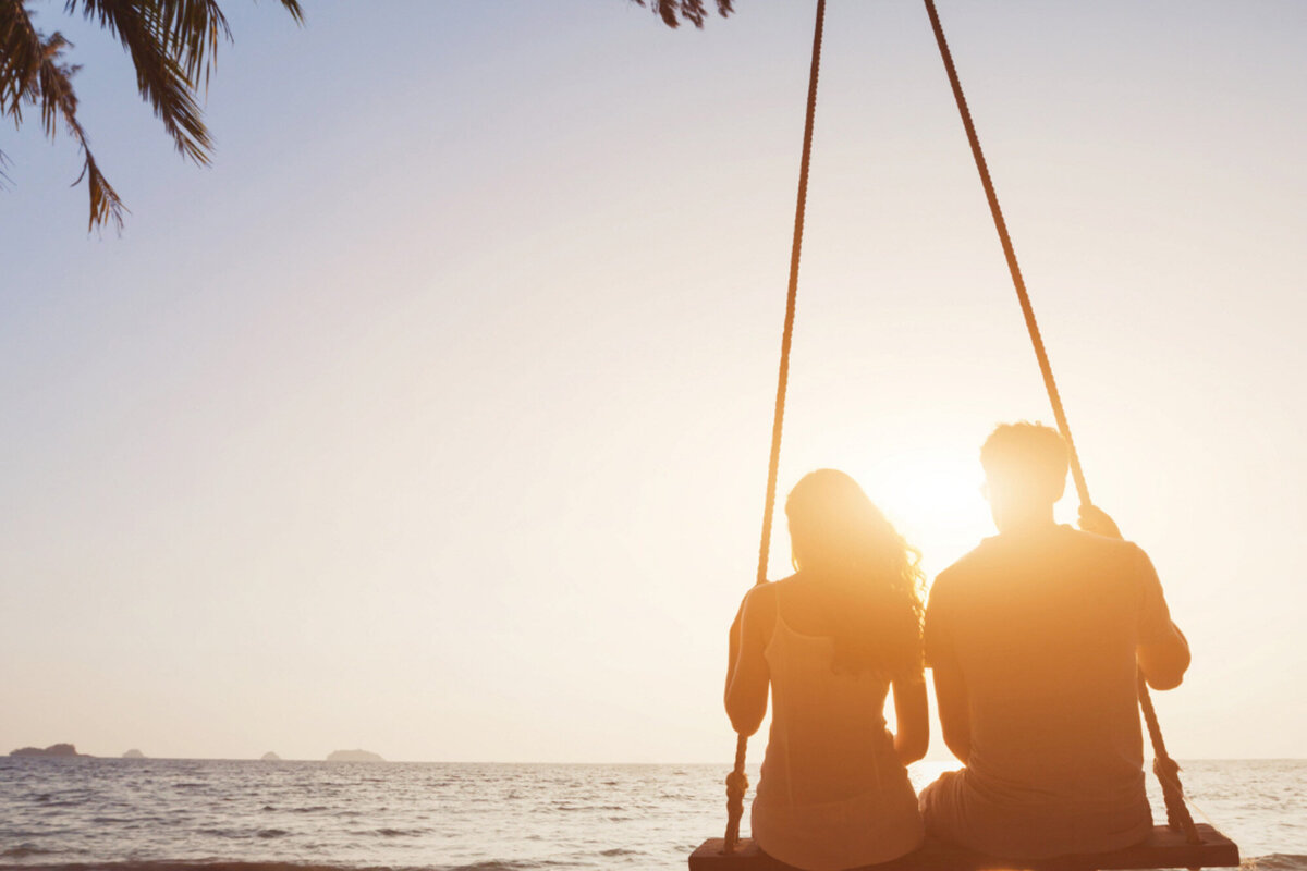 Couple sitting on the hammock at the seaside while looking at the sun