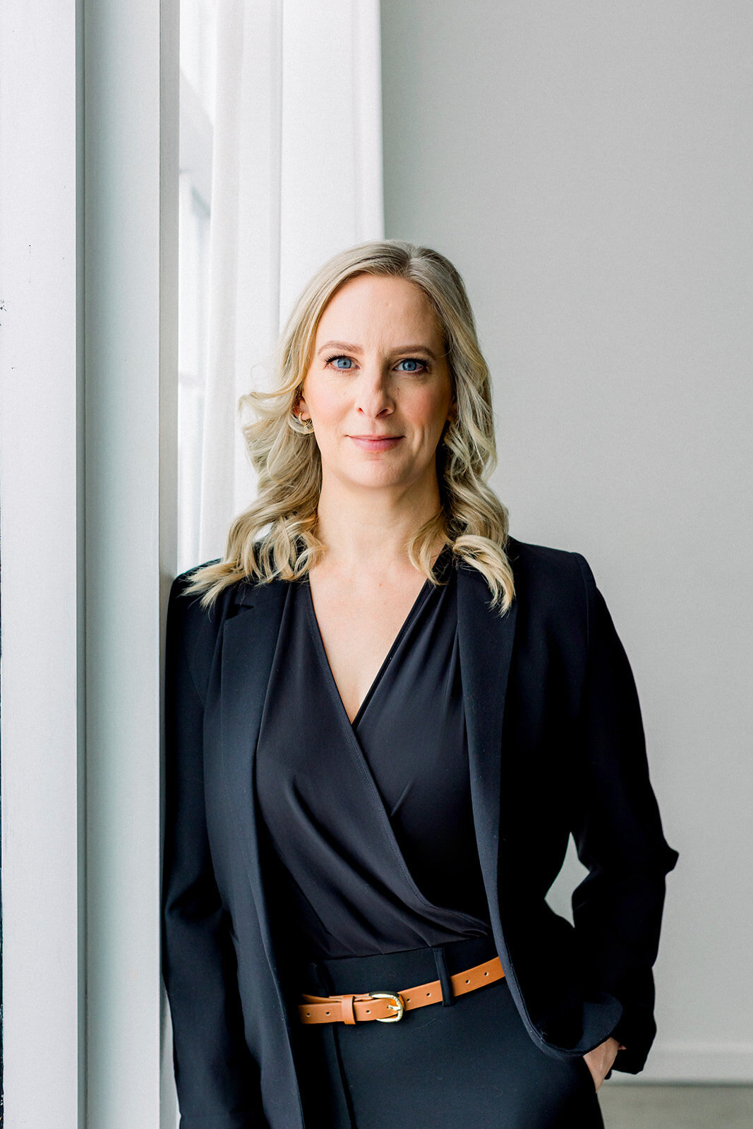 Calgary business woman with blonde hair  leaning against a window.