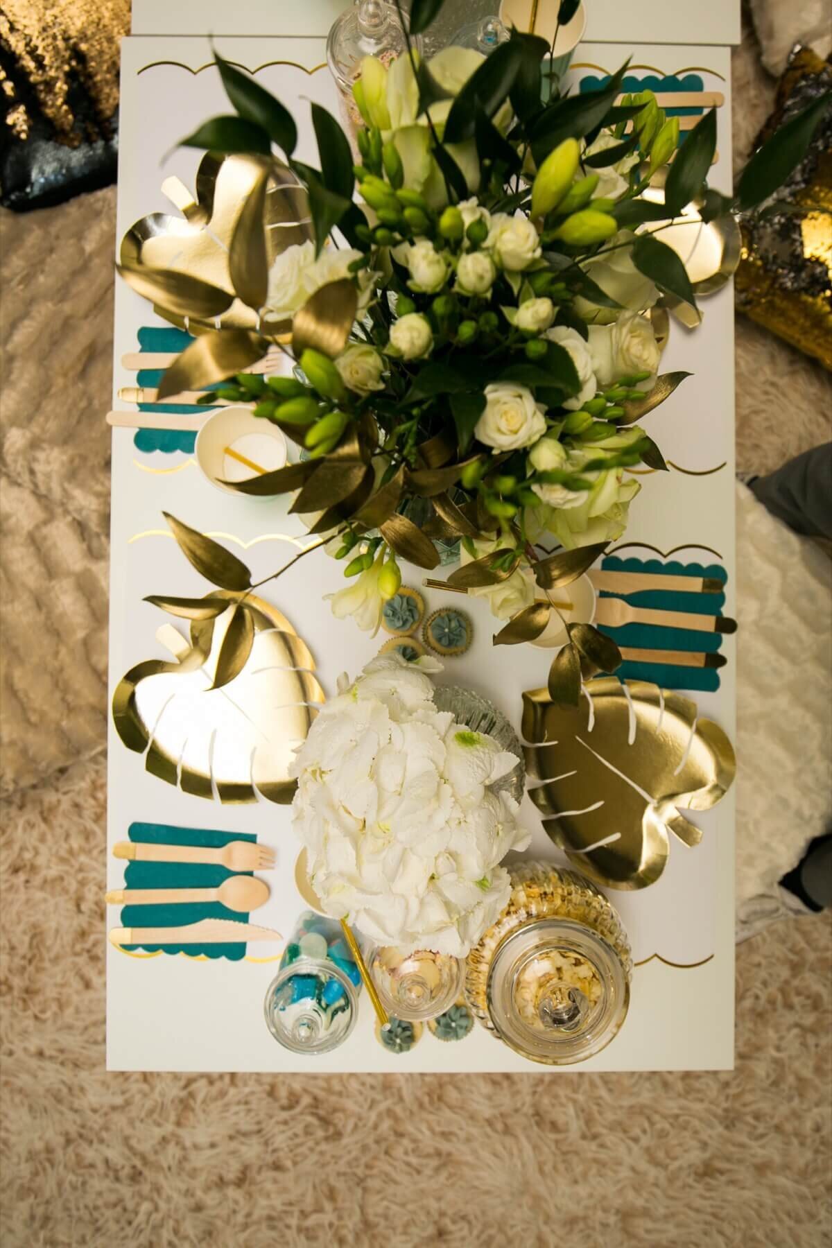 Gold and white children's table setting with sweet jars, flowers and gold leaf plates