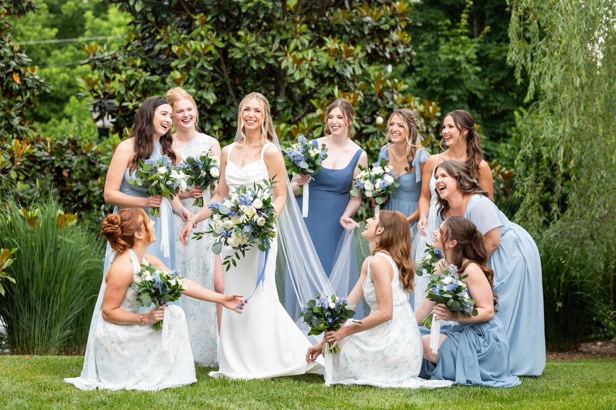 Spring wedding at WinMock at Kinderton, designed by Charming Carolina — bride and bridesmaids posing with dusty blue and greenery bouquets outside the venue’s barn.