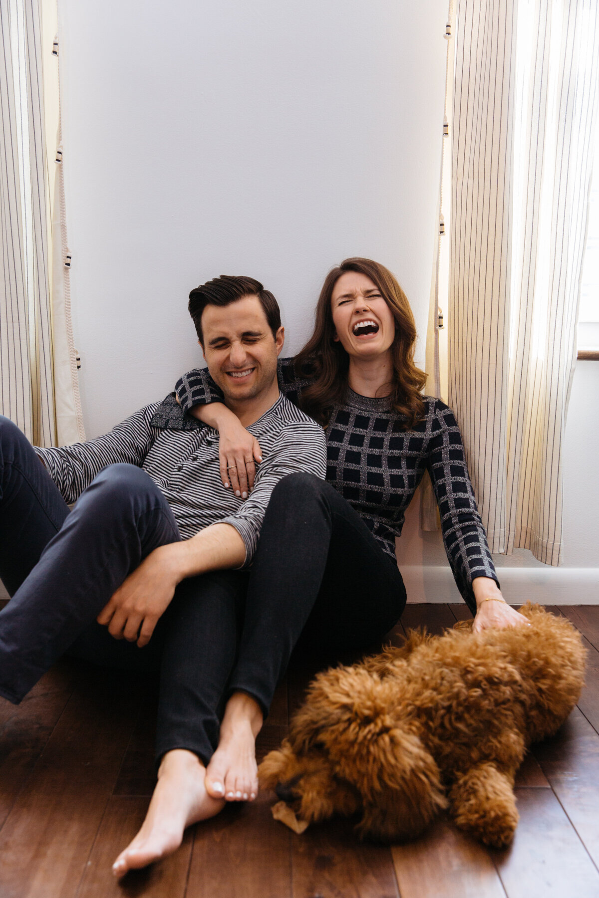 Couple sitting on the floor laughing with their dog next to them.