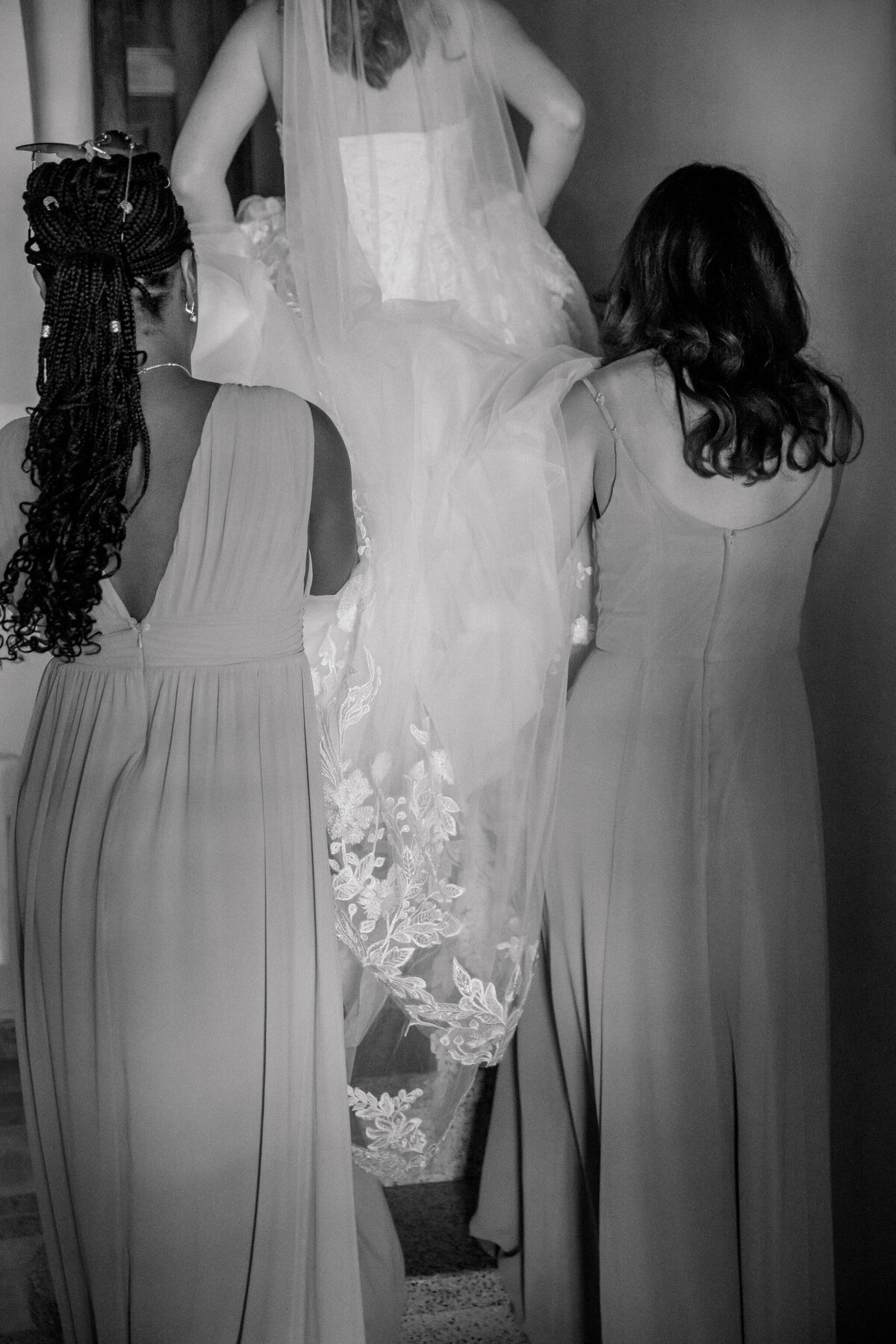 Destination Wedding in Spain | A black and white image of bridesmaids helping the bride carry her dress up the stairs of her getting ready suite.