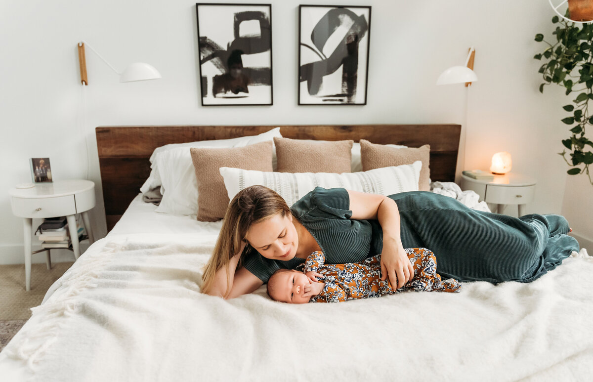 Newborn Photographer, a baby lays on bed, mom lays beside her in admiration