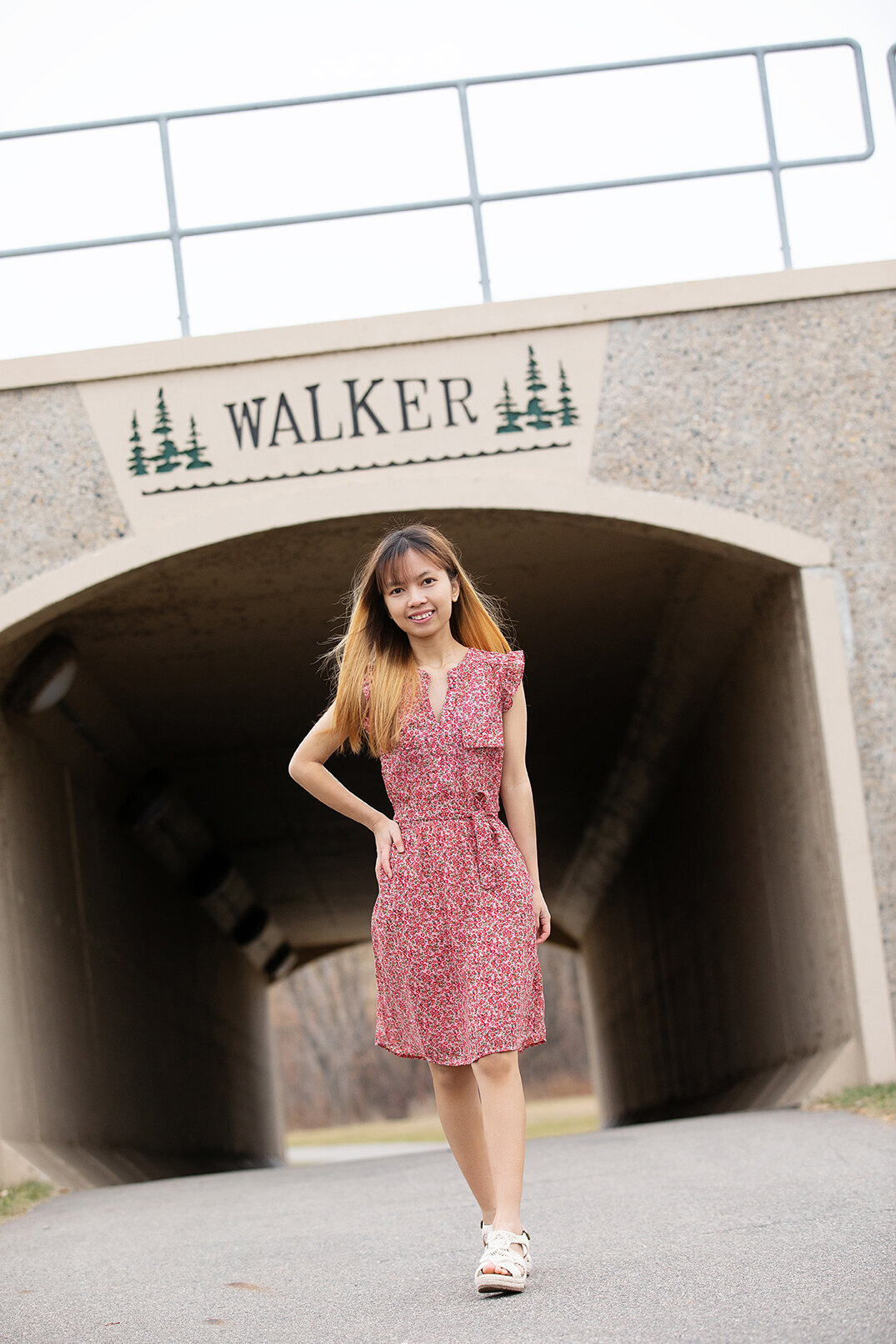 High School senior girl wearing pink dress walking towards camera outdoors with tunnel behind her Walker, Minnesota.