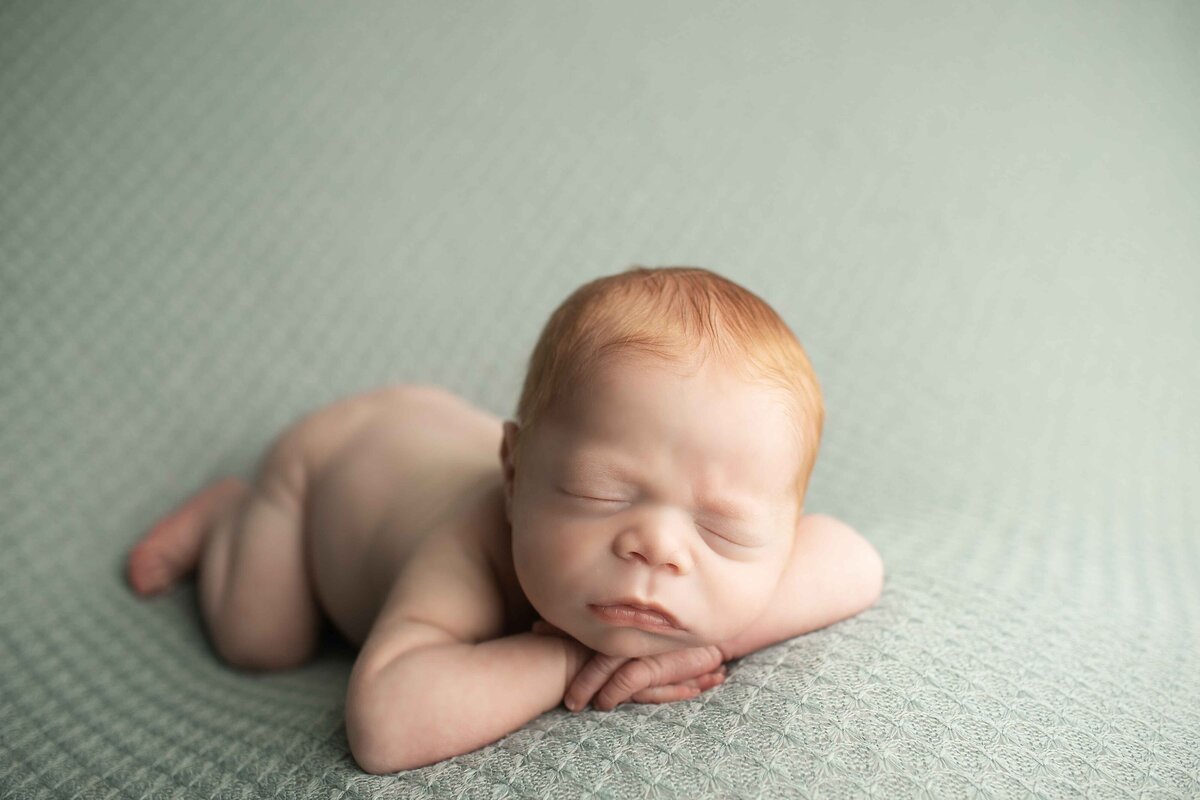 Sweet newborn boy with beautiful red hair wrapped snugly and posed on a textured backdrop, exuding warmth and innocence