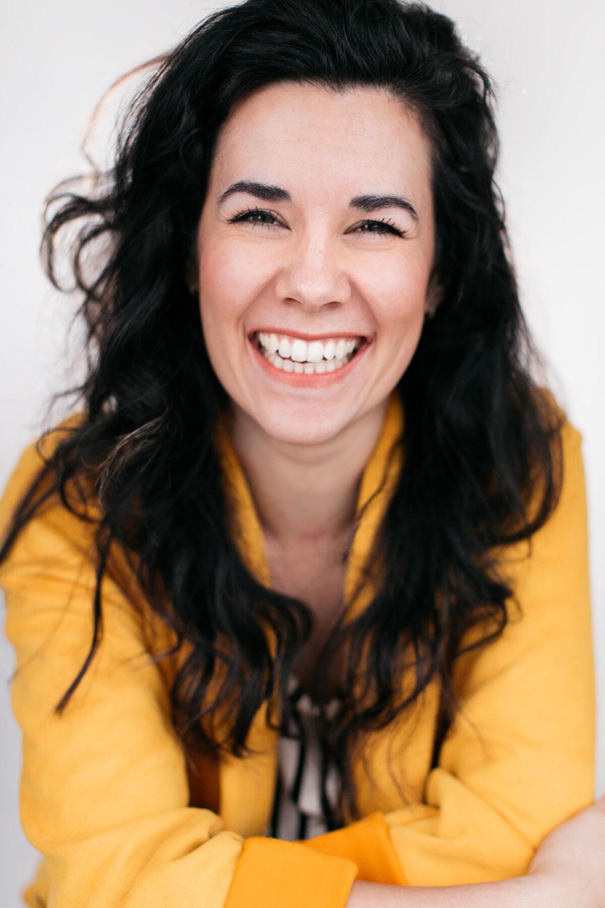 Castingfoto van Natasha Schalker. Vrouw met zwart haar in gele top voor lichtgrijze achtergrond.