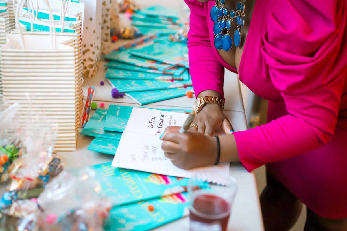 Woman in hot pink suit signing card at a celebration event