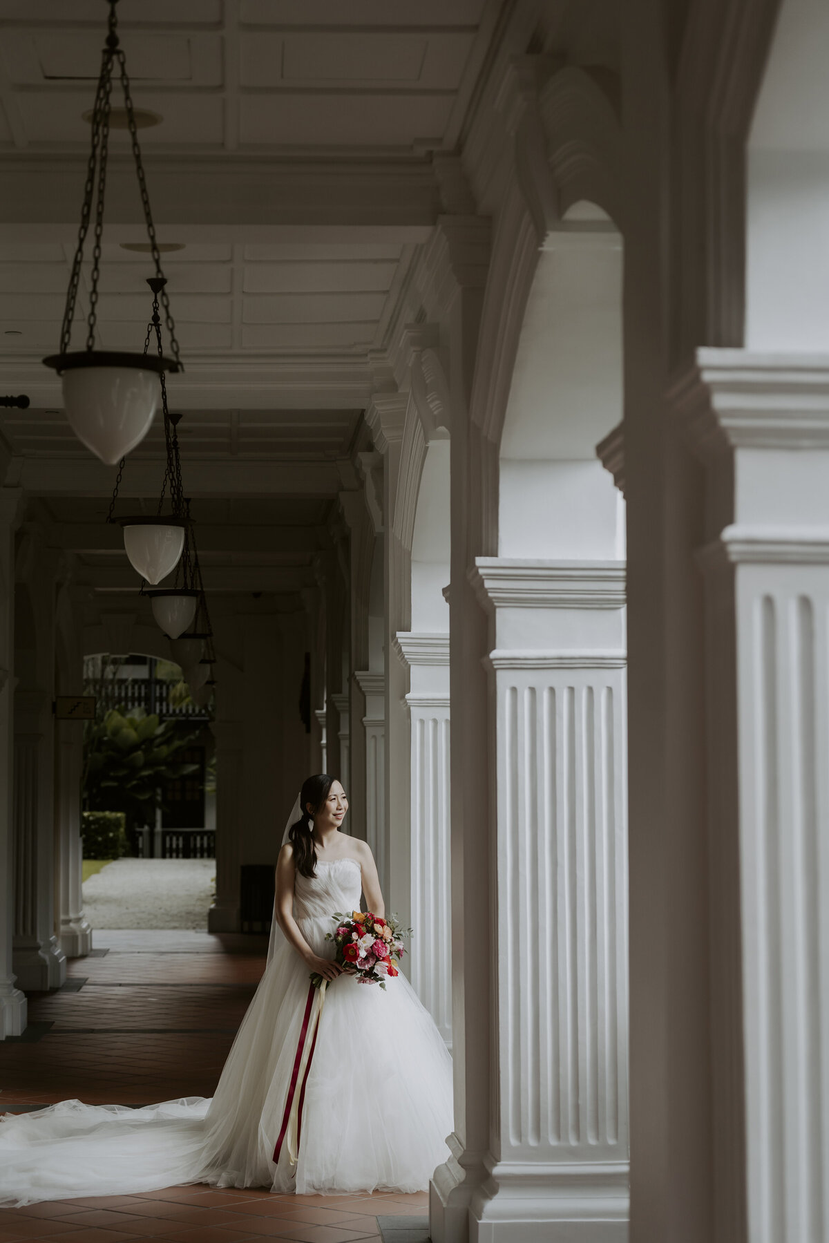 the bride wearing a wedding dress stands between white pillars at the raffles hotel